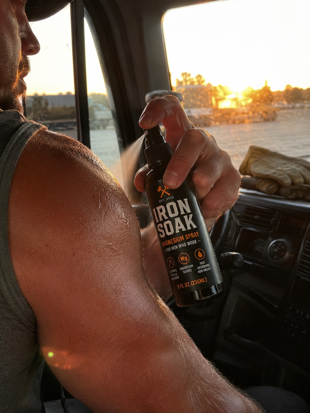 Man spraying Iron Soak magnesium spray on sore shoulder in work truck at sunset